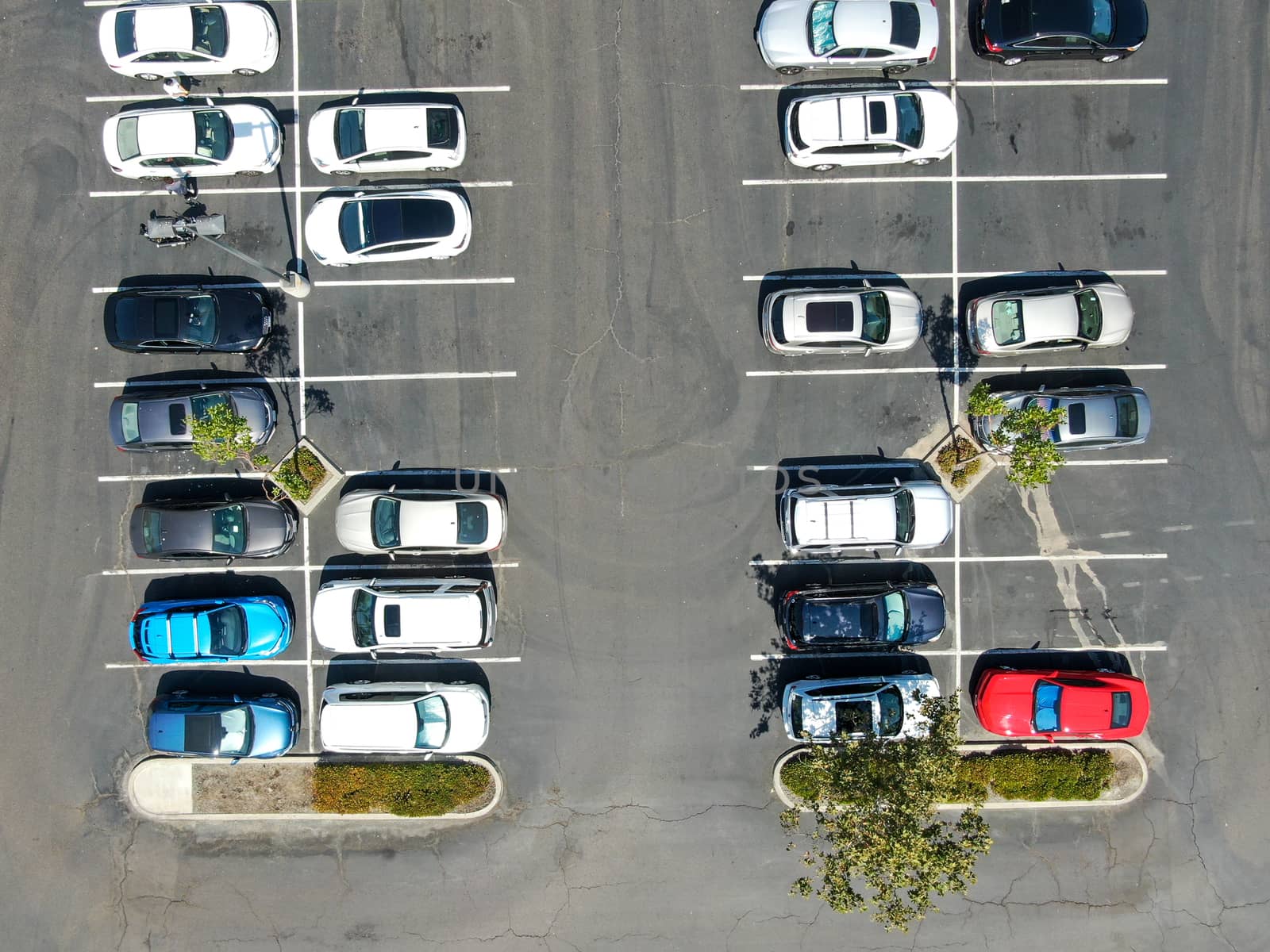 Aerial top view of parking lot at shopping mall with varieties of colored vehicles. People walking to their car and trying to park.