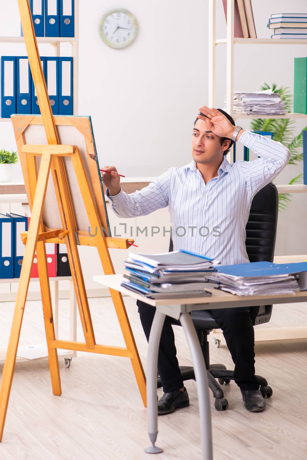 Young handsome employee enjoying painting at the office 