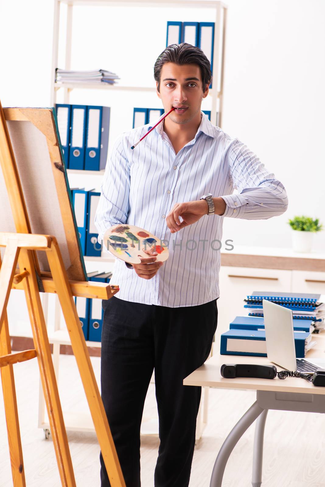 Young handsome employee enjoying painting at the office 