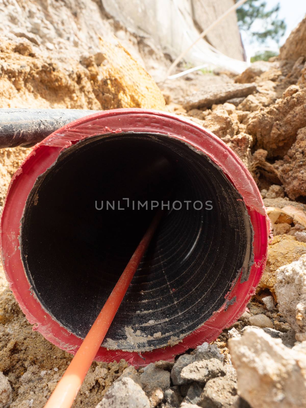 Detail of optic fiber wire in ribbed flexible red plastic tube, thin trench at lamp post 
