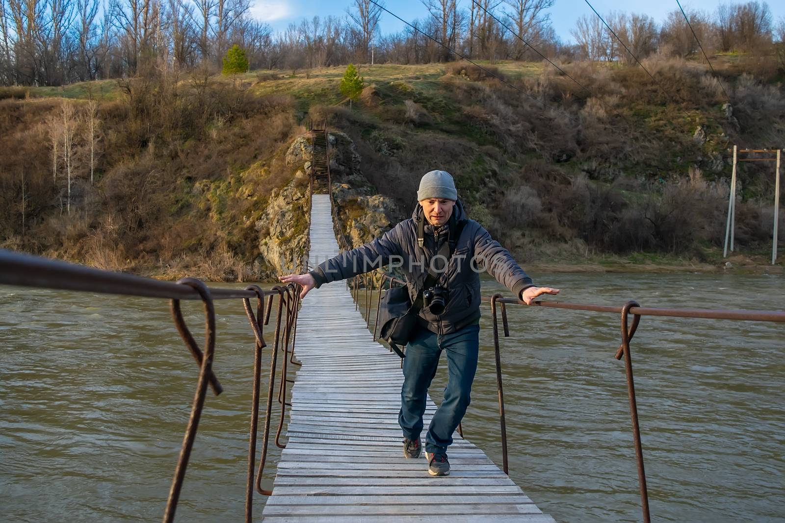 autumn, a man, a photographer, is afraid and runs over a swaying suspension bridge over a river