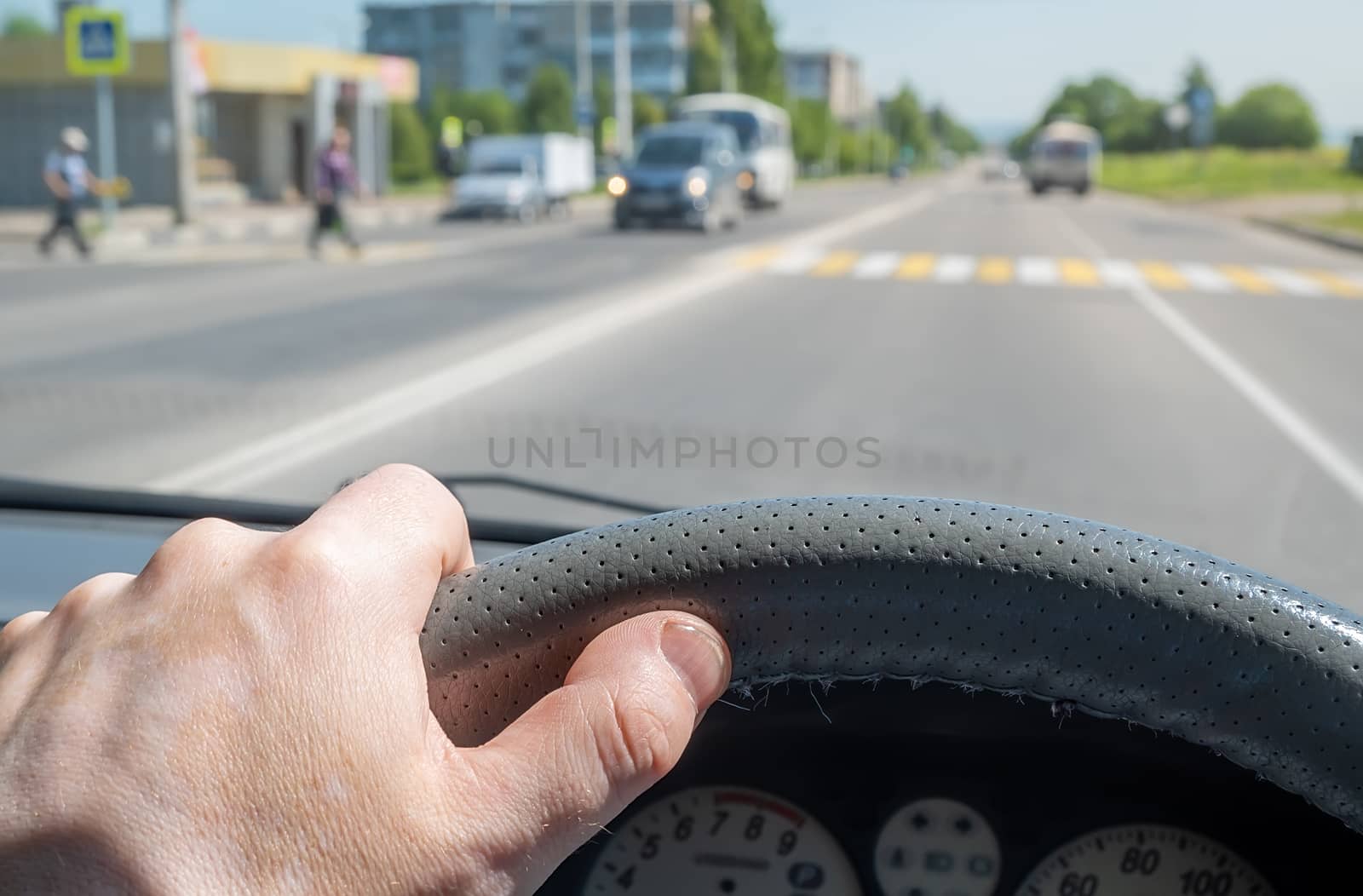 the driver hand on the steering wheel of a car approaching a pedestrian crossing where pedestrians