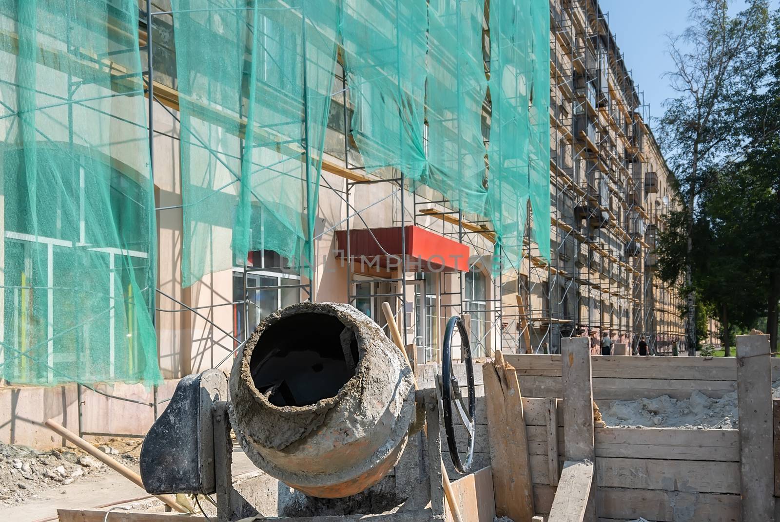 an industrial construction concrete mixer and a box of cement stand on the street against the background of a multi-storey building where the facade is being repaired