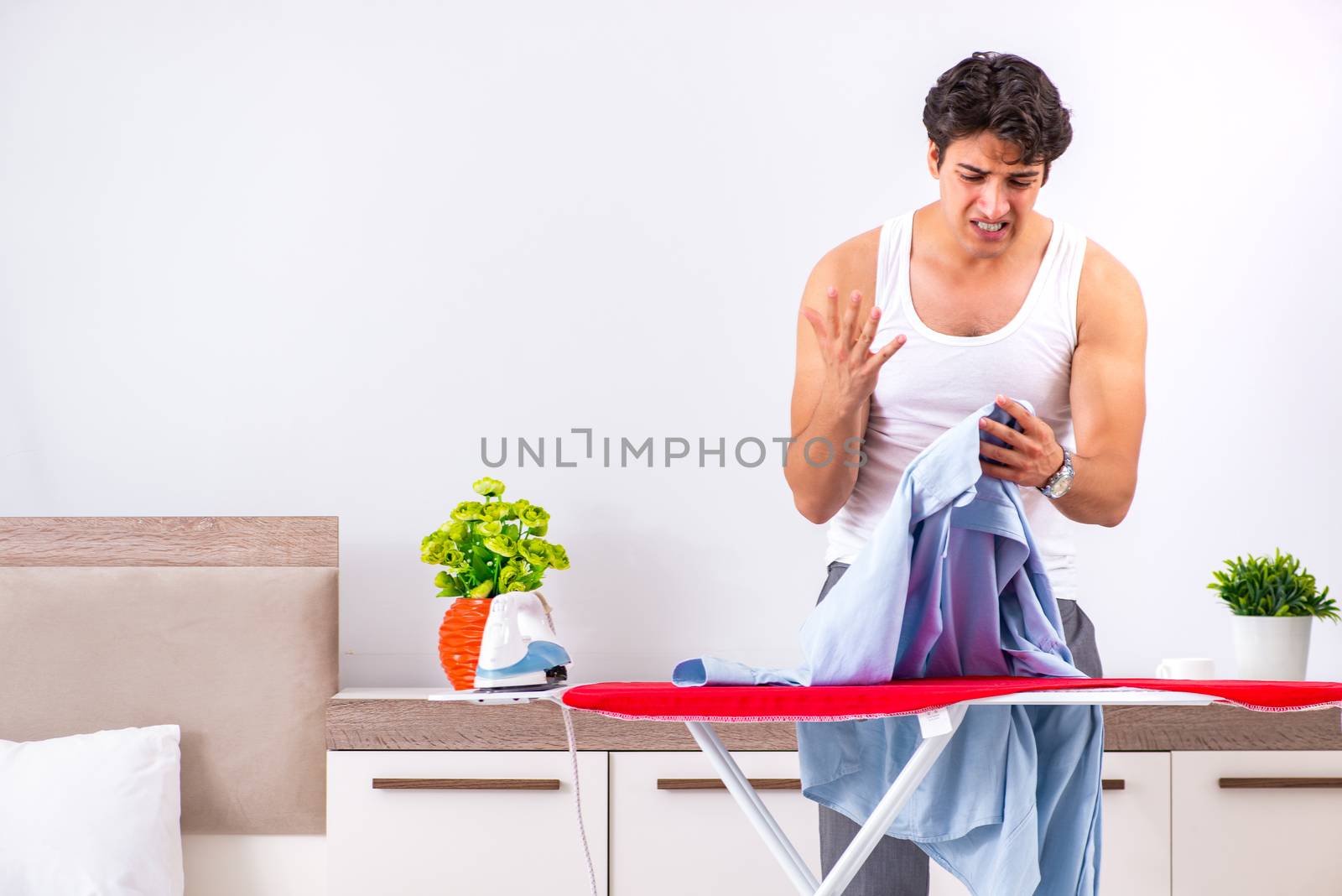 Young man ironing in the bedroom 