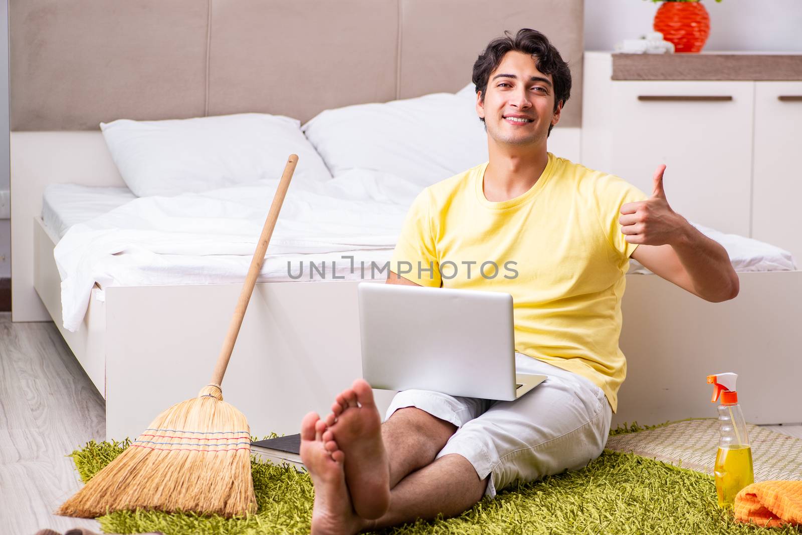 Young handsome man cleaning the bedroom and sitting at the computer