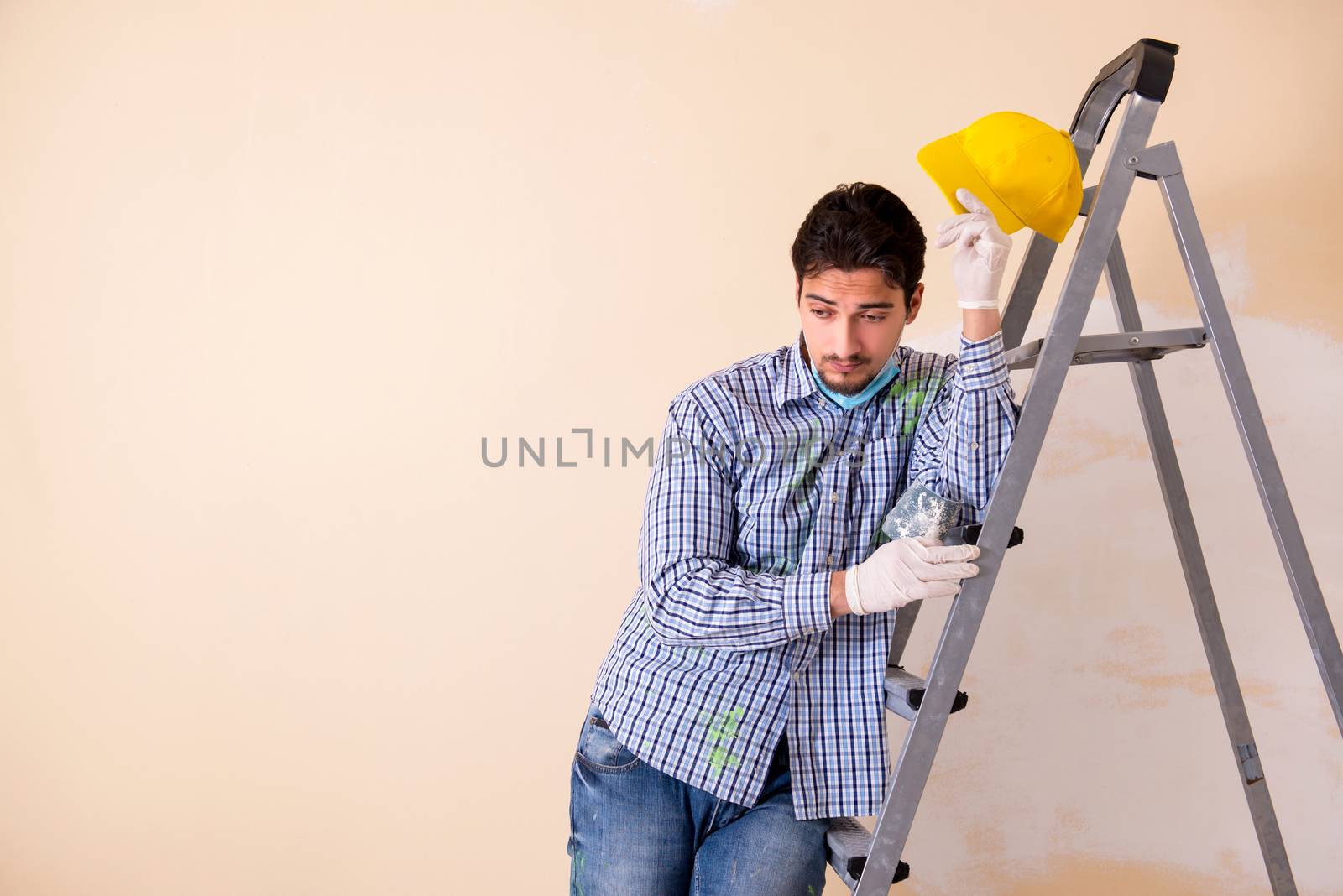 Young contractor sanding wall down with sandpaper 
