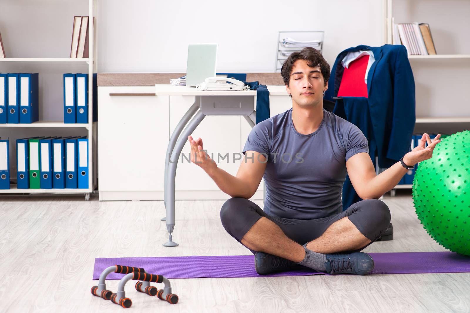 Young male employee exercising in the office by Elnur