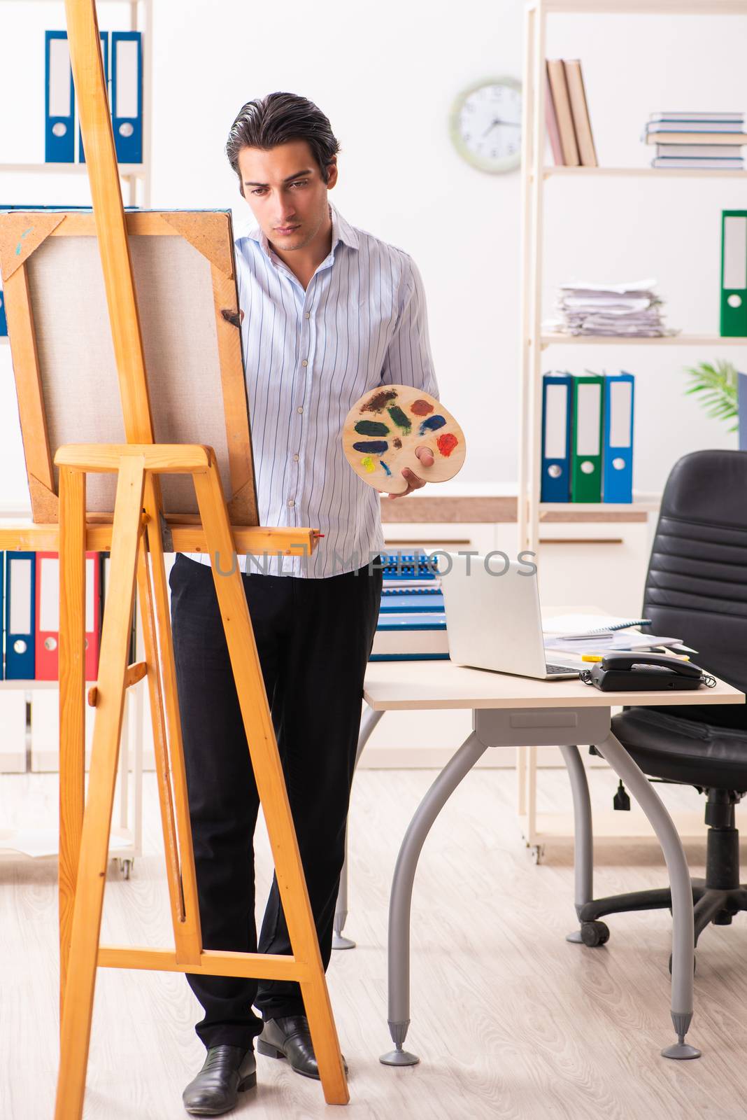 Young handsome employee enjoying painting at the office  by Elnur
