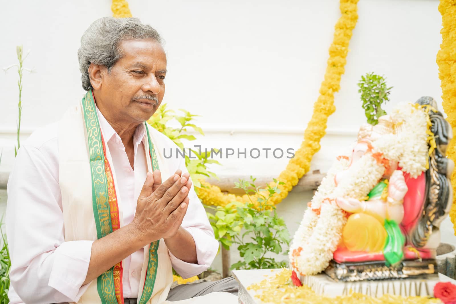 Elder man offering Bhajan or hymn in front of Lord Ganesha Idol during Ganesha or vinayaka Chaturthi festvial ceremony at home