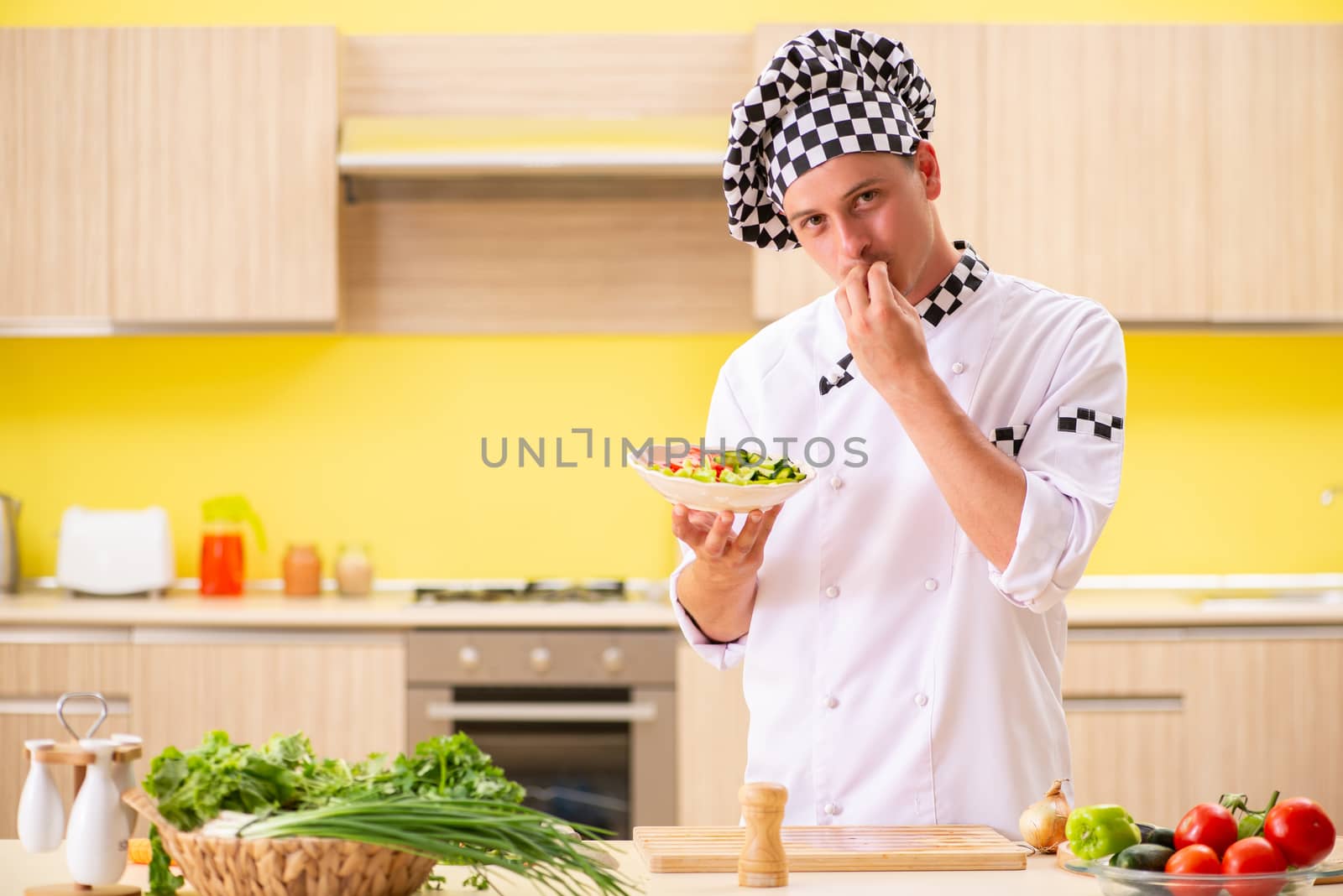 Young professional cook preparing salad at kitchen