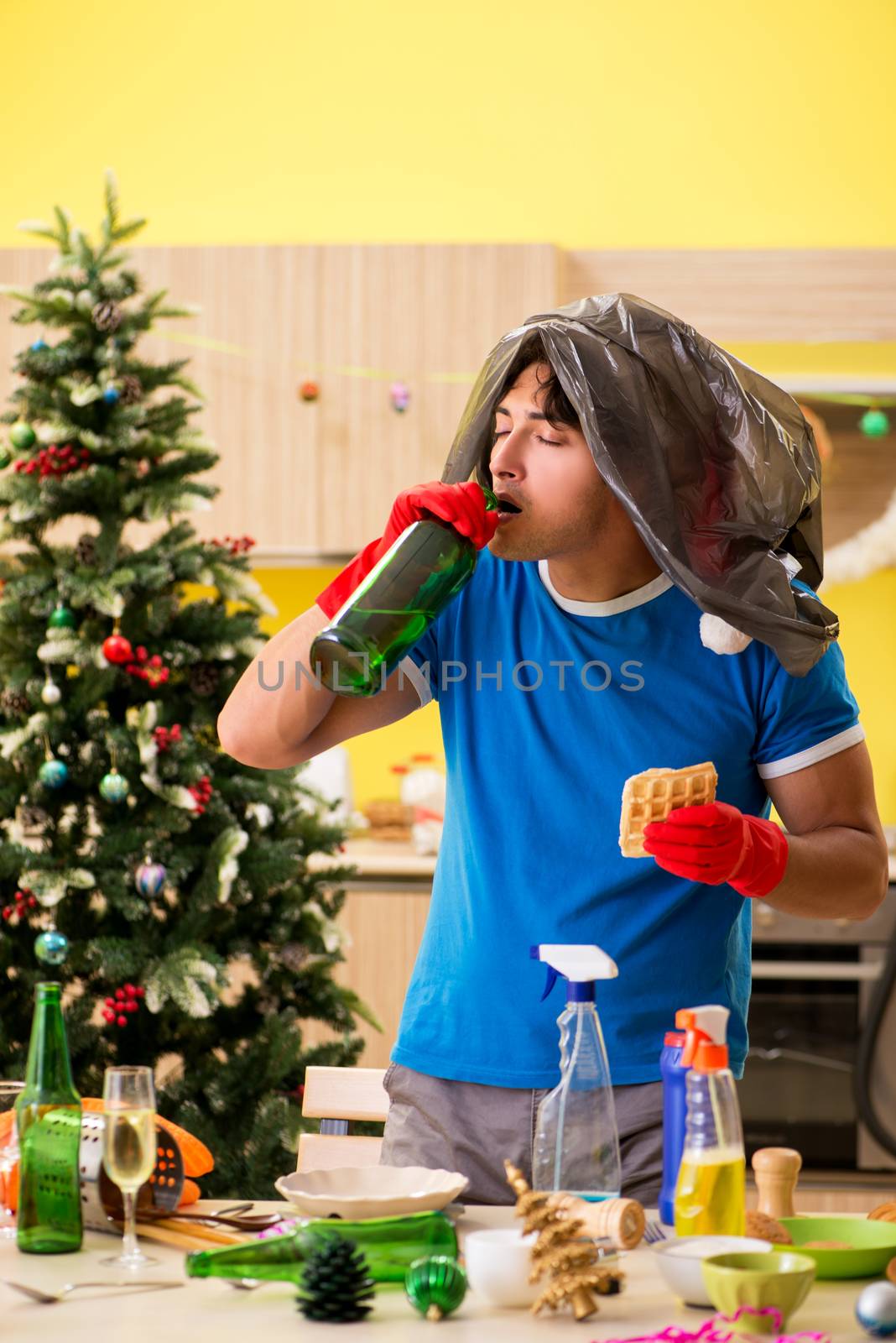 Young man cleaning kitchen after Christmas party  by Elnur