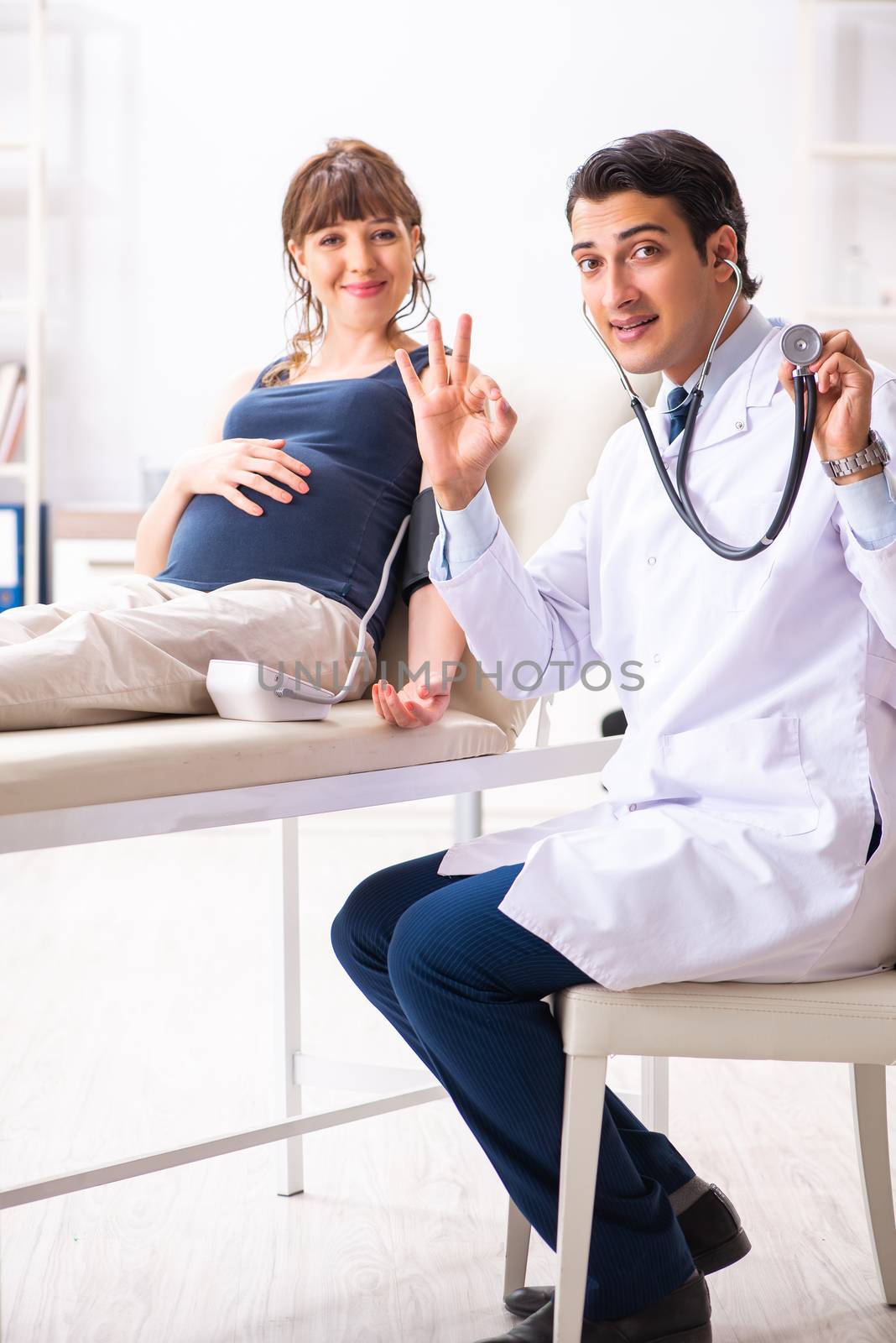 Young doctor checking pregnant woman's blood pressure by Elnur