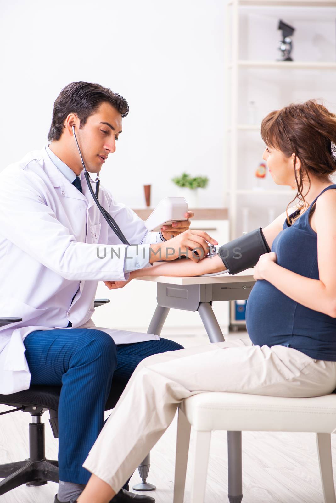 Young doctor checking pregnant woman's blood pressure