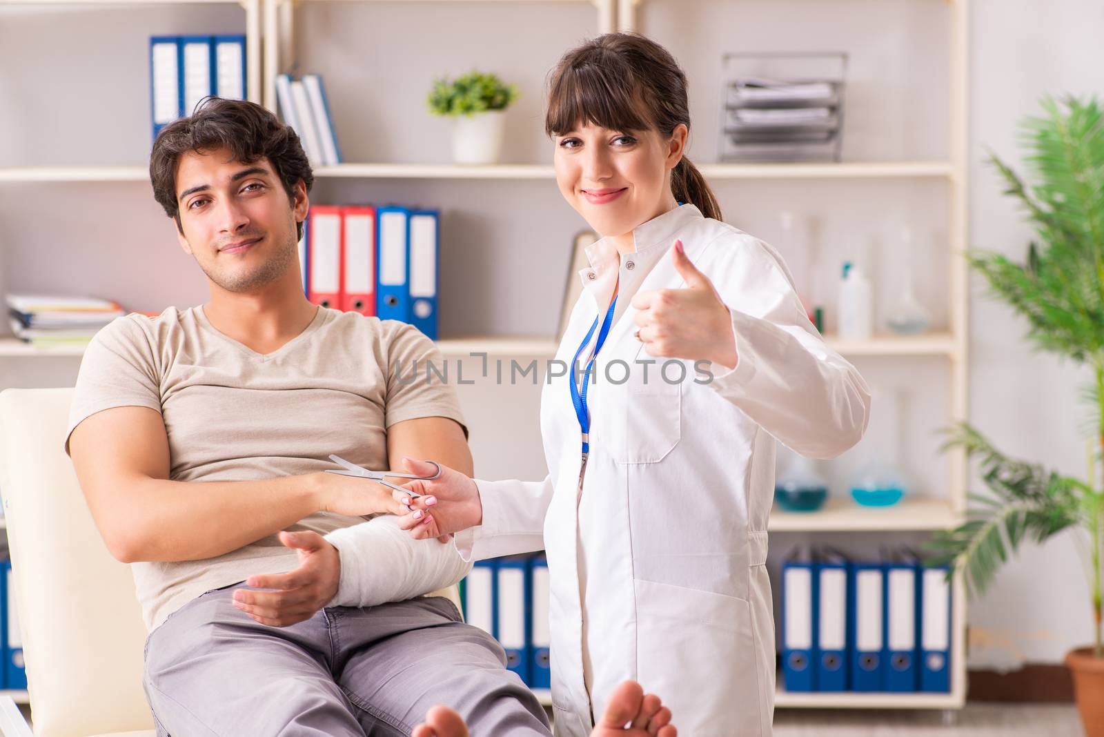 Young man with bandaged arm visiting female doctor traumatologis by Elnur