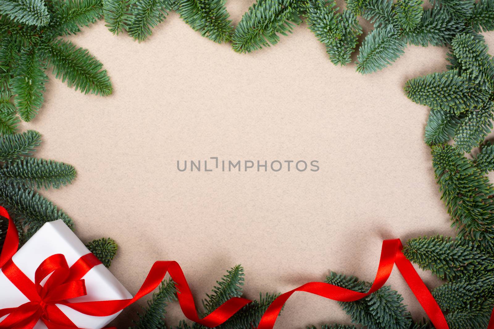 Christmas noble fir tree twigs and gift with red ribbon on brown paper background with copy space for text