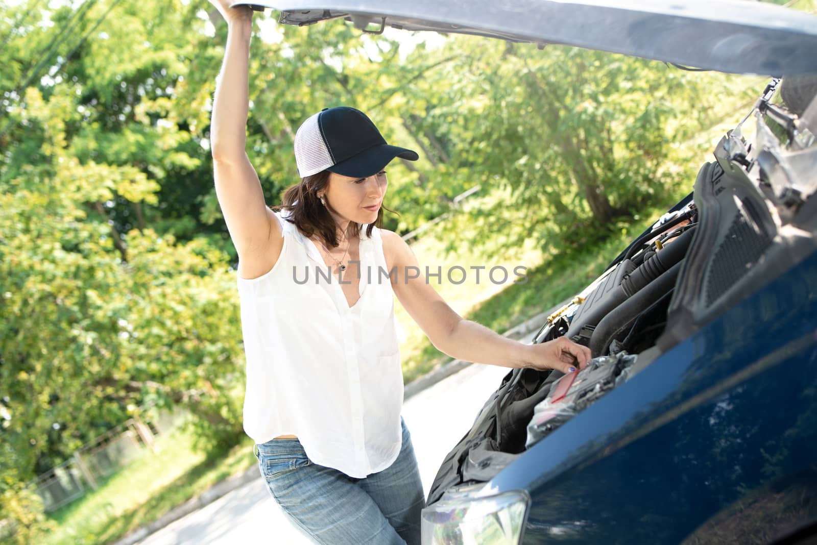 A woman waits for assistance near her car broken down on the road side.