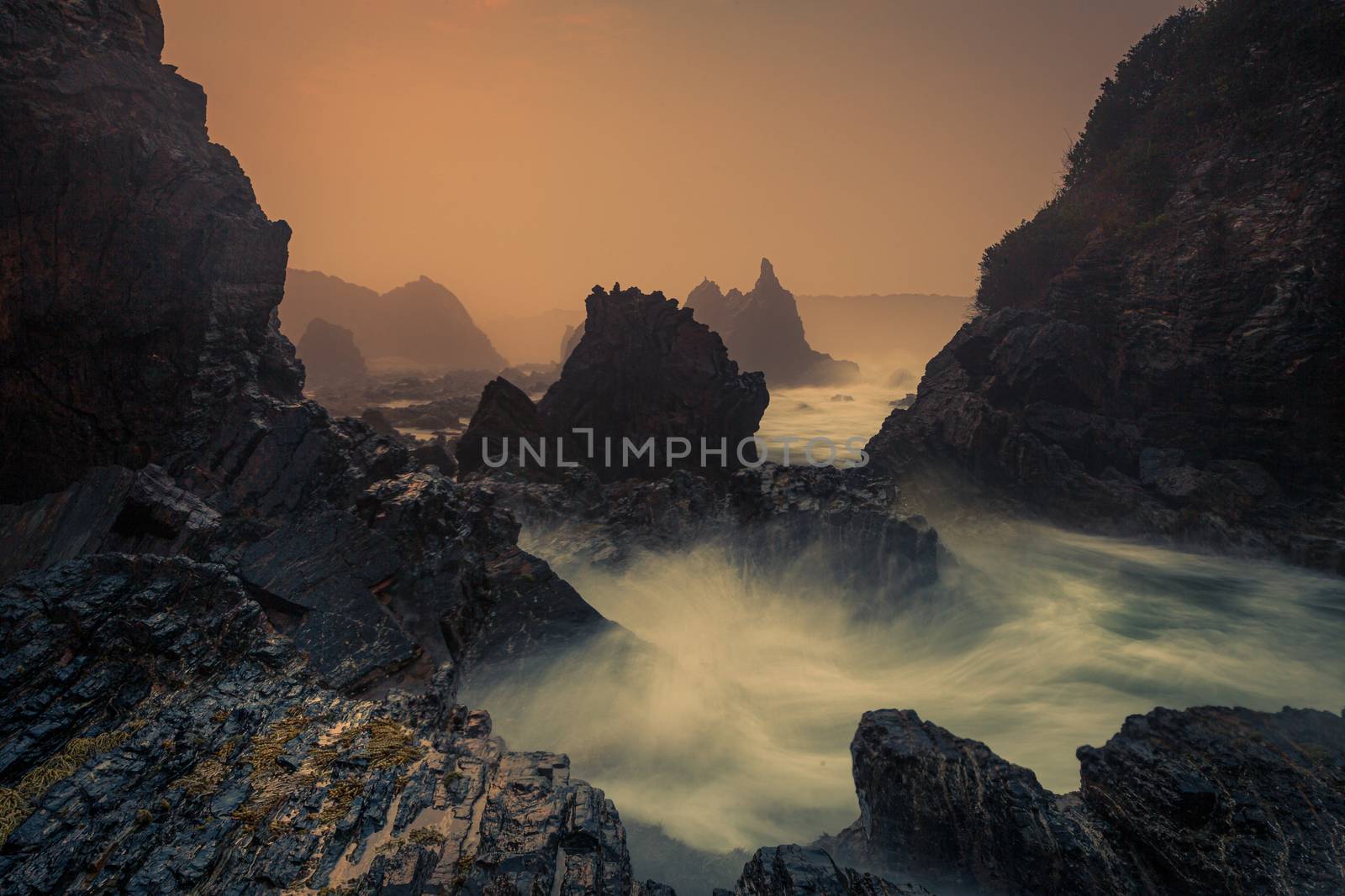 Mystical sea fog, sea spray and sunrise on the sharp craggy volcanic rock coastline 