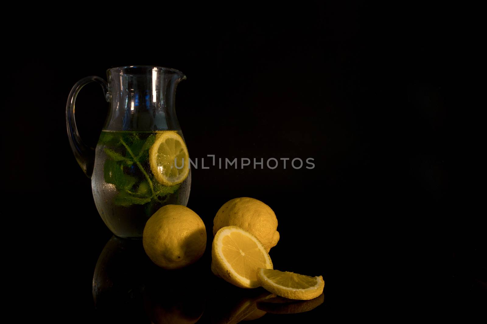 still life with a jug of water filled with mint and lemon with the raw lemon fruit in the foreground