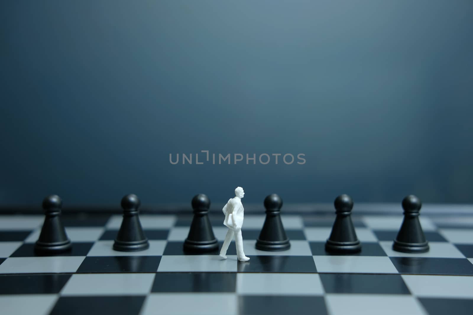 Miniature of businessman walking above black pawn on a chessboard. image photo