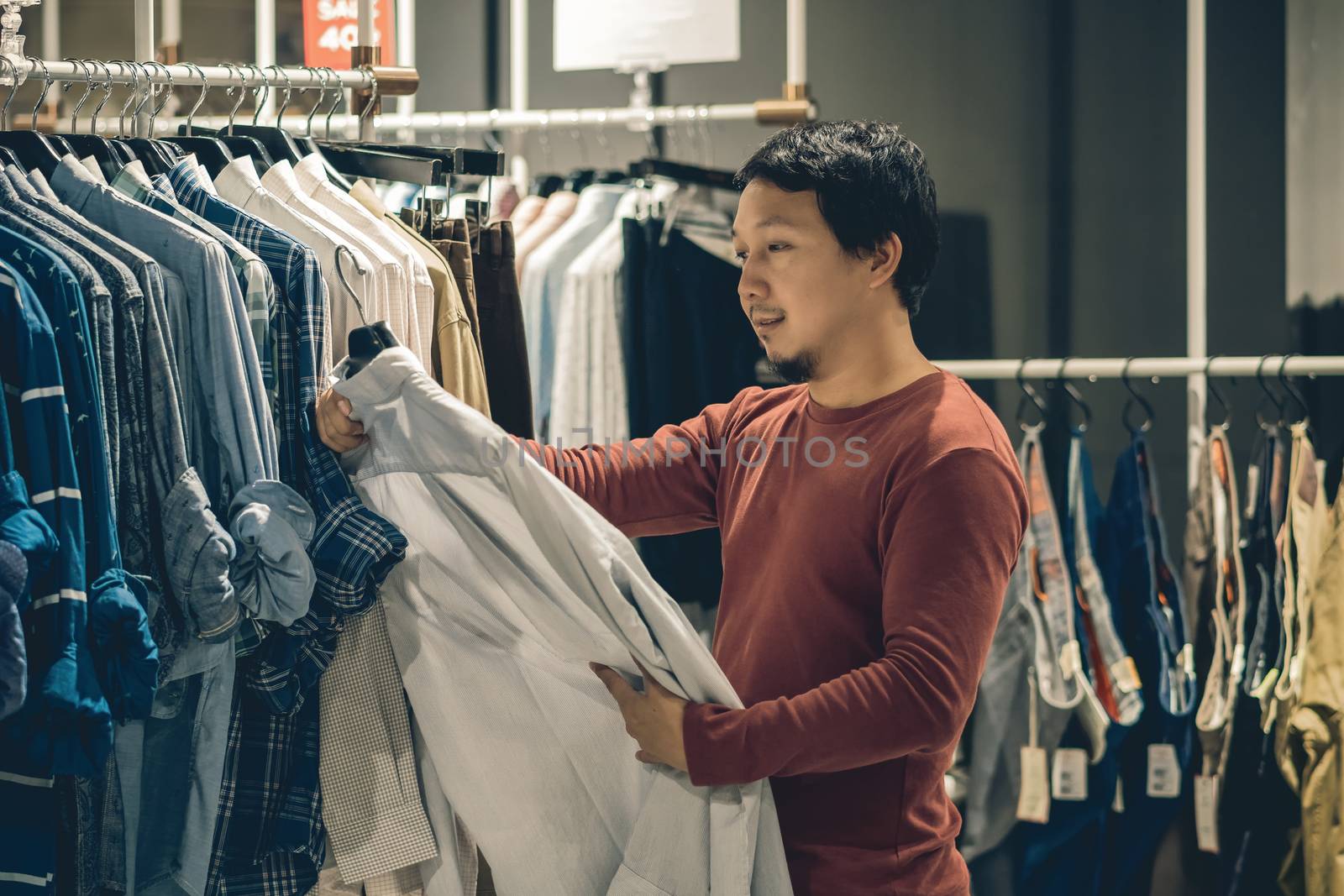 Smart asian man with beard choosing clothes in clothing store at by Tzido