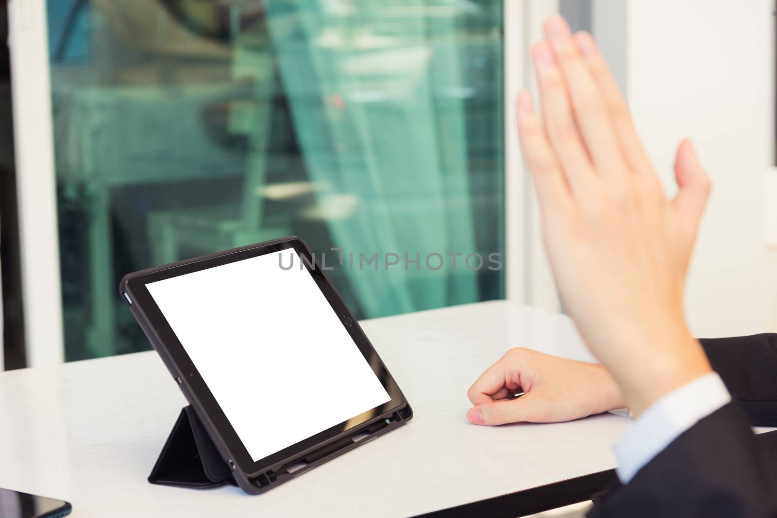 Work from home, Back view of Asian young businessman smile wearing suit video conference call or facetime by smart digital tablet computer blank screen raise hand say hello to teammates on desk