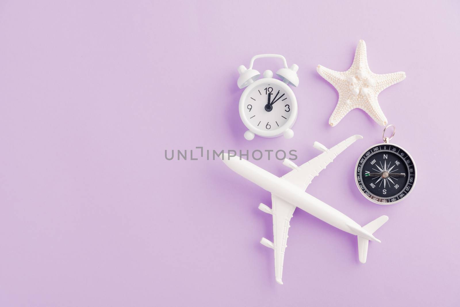 World Tourism Day, Top view flat lay of minimal toy model plane, airplane, starfish, alarm clock and compass, studio shot isolated on a purple background, accessory flight holiday concept