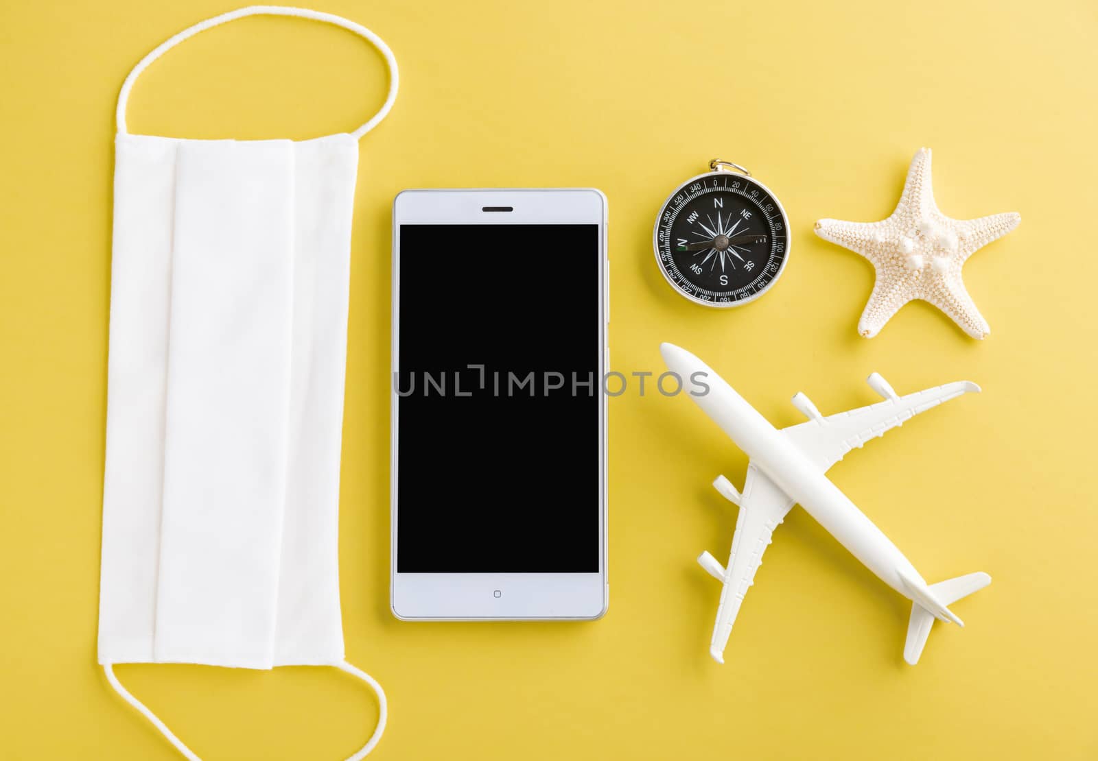 World Tourism Day, Top view of minimal model plane, airplane, starfish, compass, smartphone blank screen and face mask isolated on yellow background, accessory flight holiday under coronavirus concept