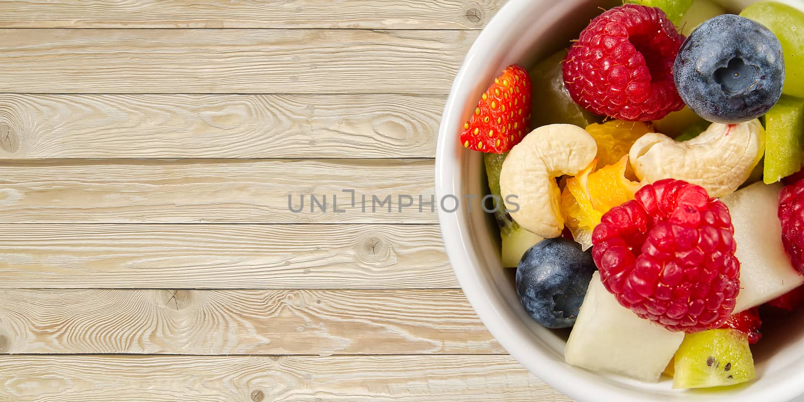 Bowl of healthy fresh fruit salad on wooden table. top view copy space. modern fruit salad light wooden background