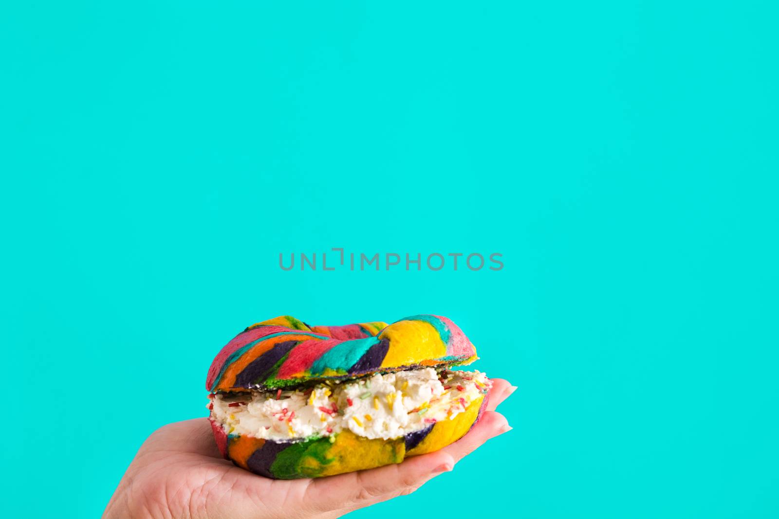 Colorful bagel with cheese and sprinkles in hand on blue background