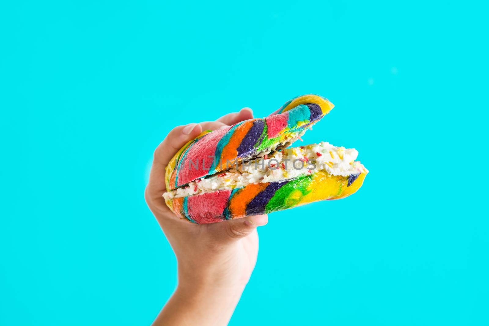Colorful bagel with cheese and sprinkles in hand on blue background by chandlervid85