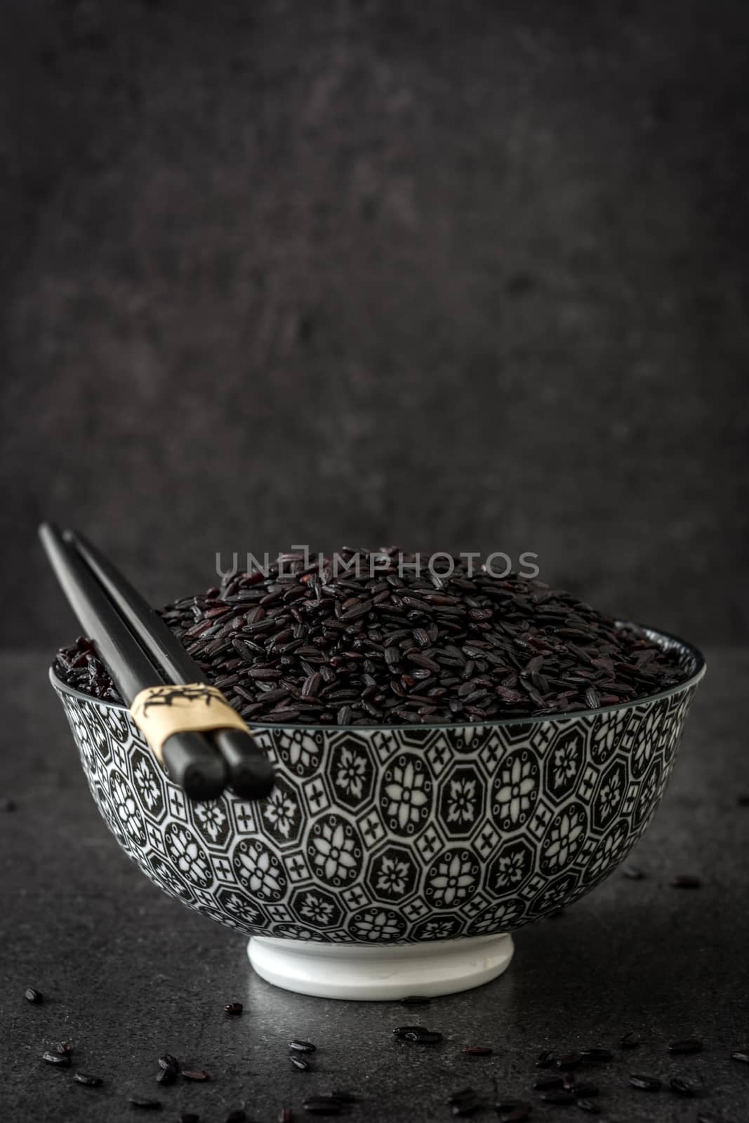 Black rice in a bowl on black background by chandlervid85