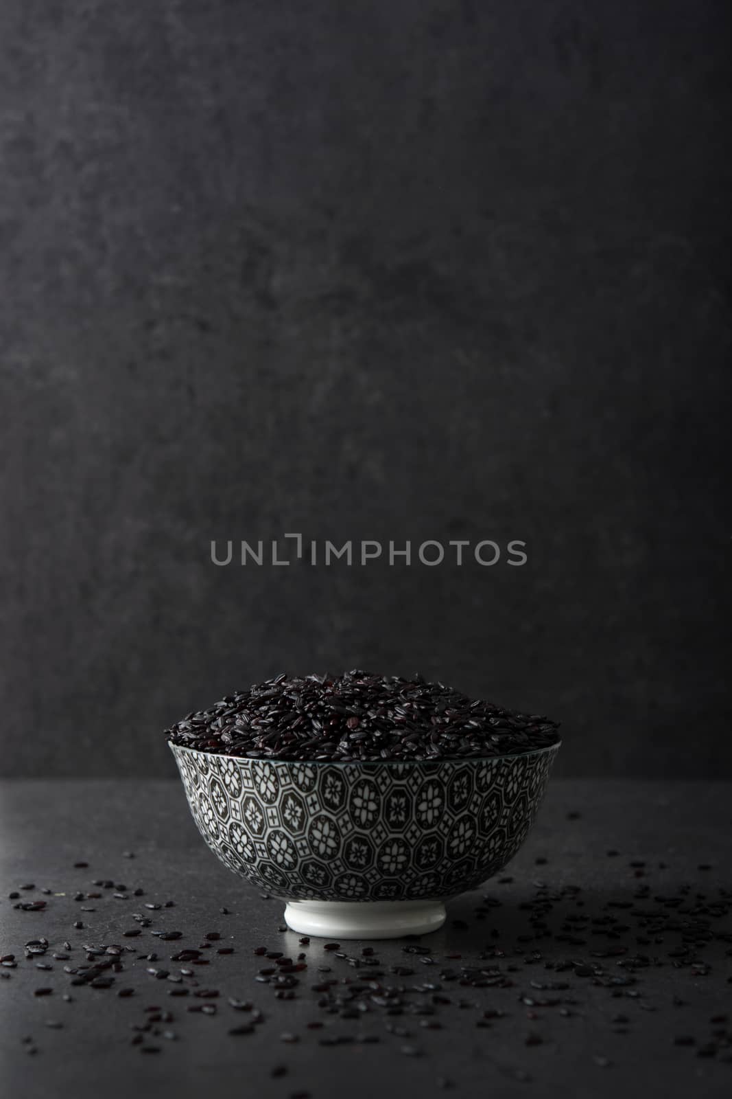 Black rice in a bowl on black background by chandlervid85