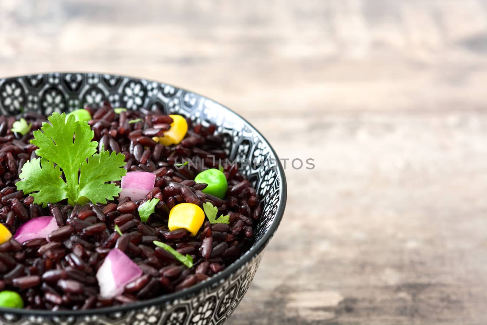 Black rice in a bowl and vegetables on wooden table by chandlervid85