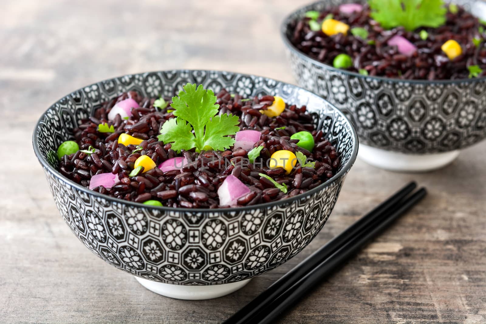 Black rice in a bowl and vegetables on wooden table by chandlervid85