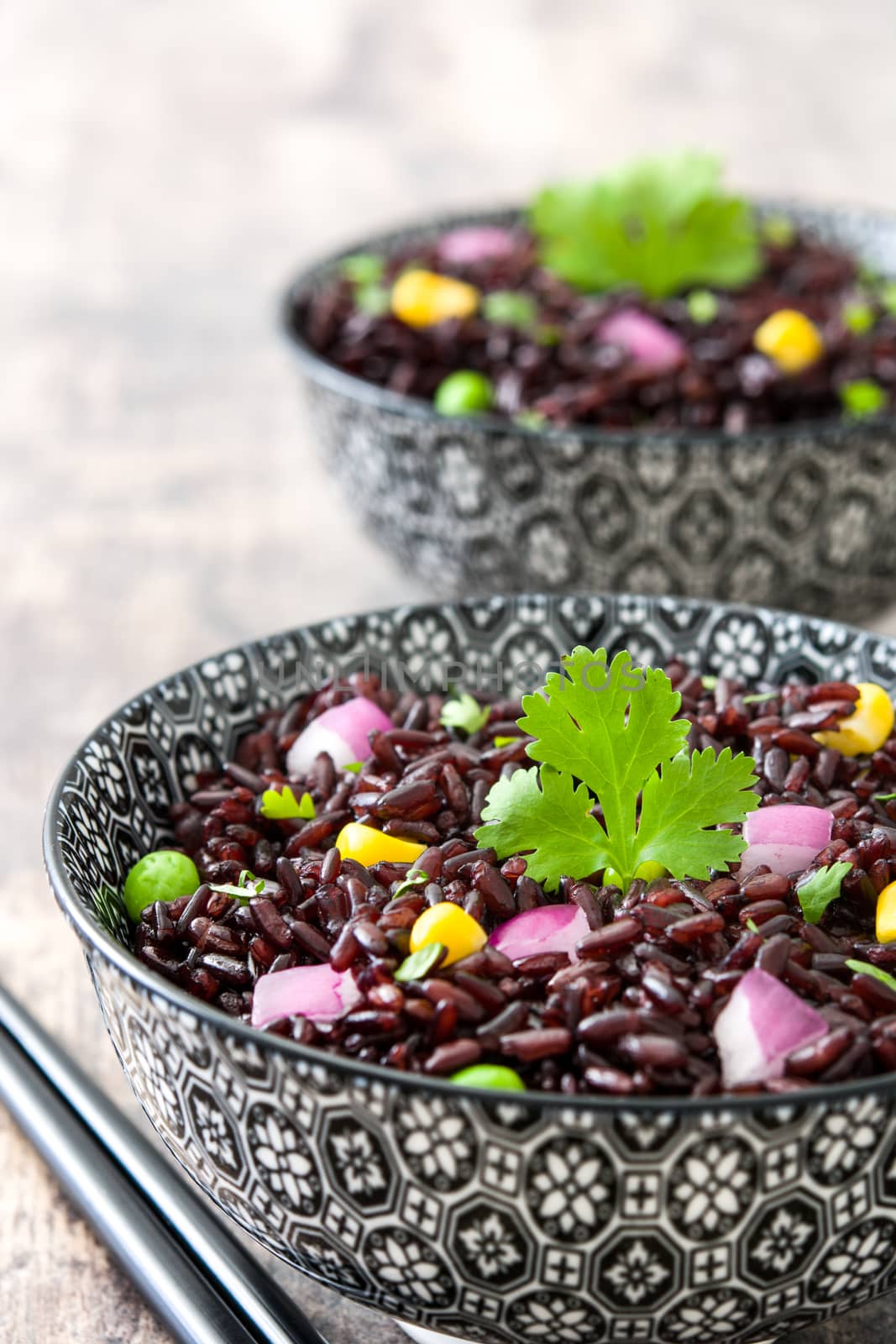 Black rice in a bowl and vegetables on wooden table