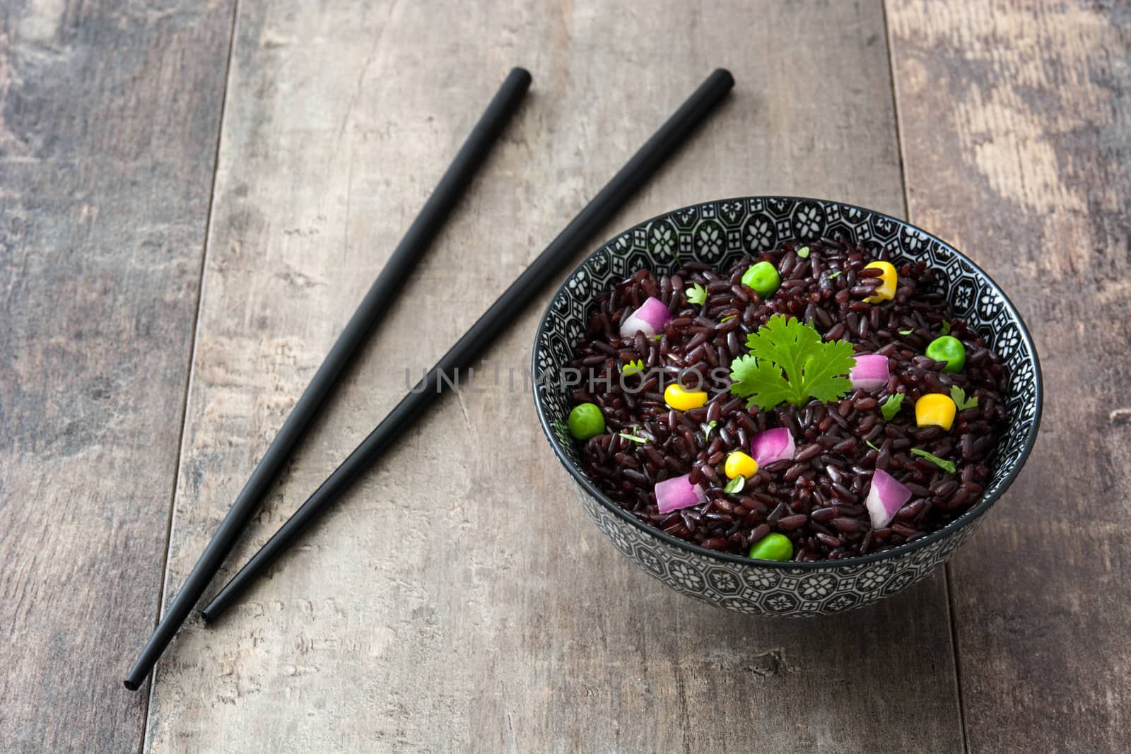 Black rice in a bowl and vegetables on wooden table by chandlervid85