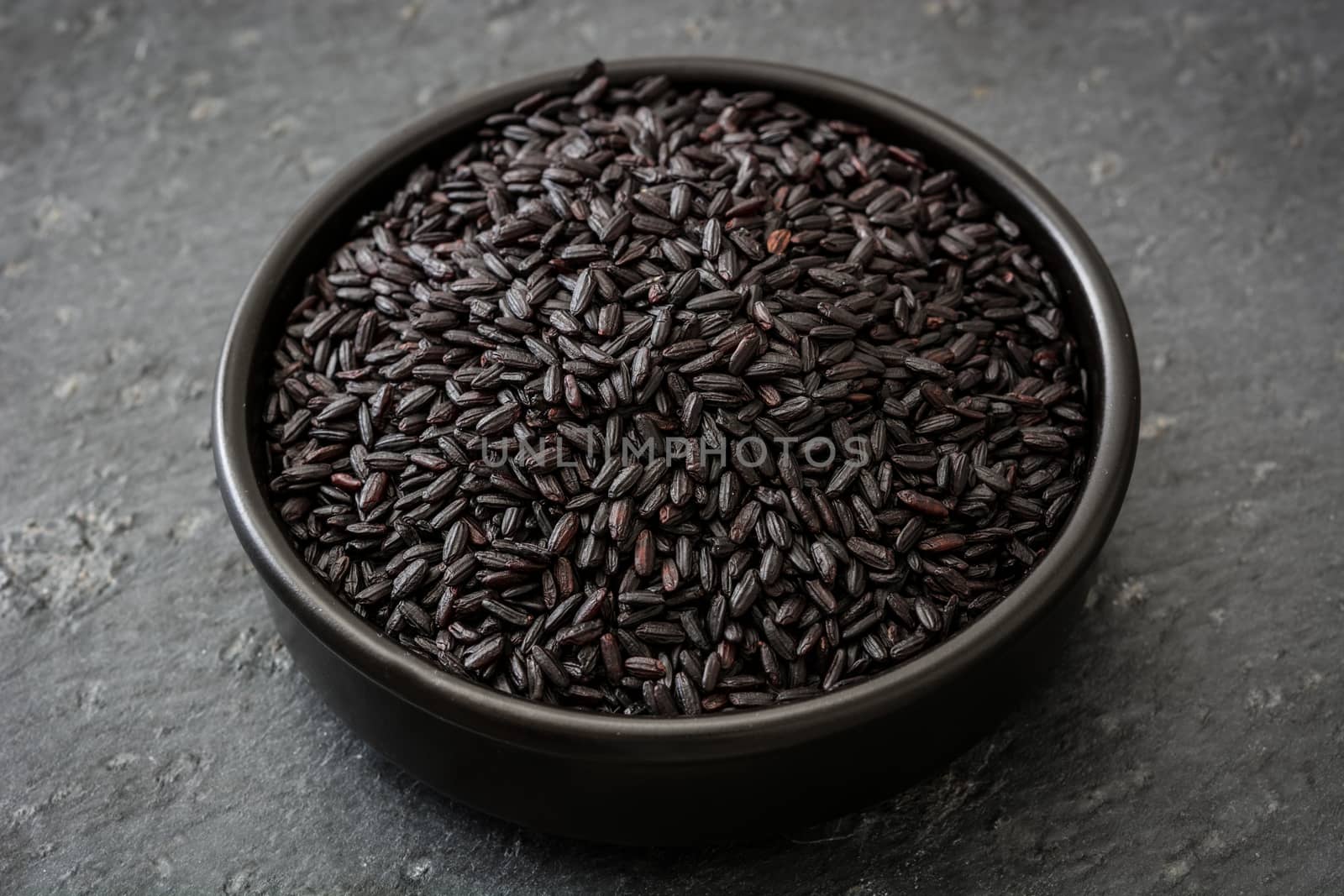 Black rice in a bowl on black background by chandlervid85