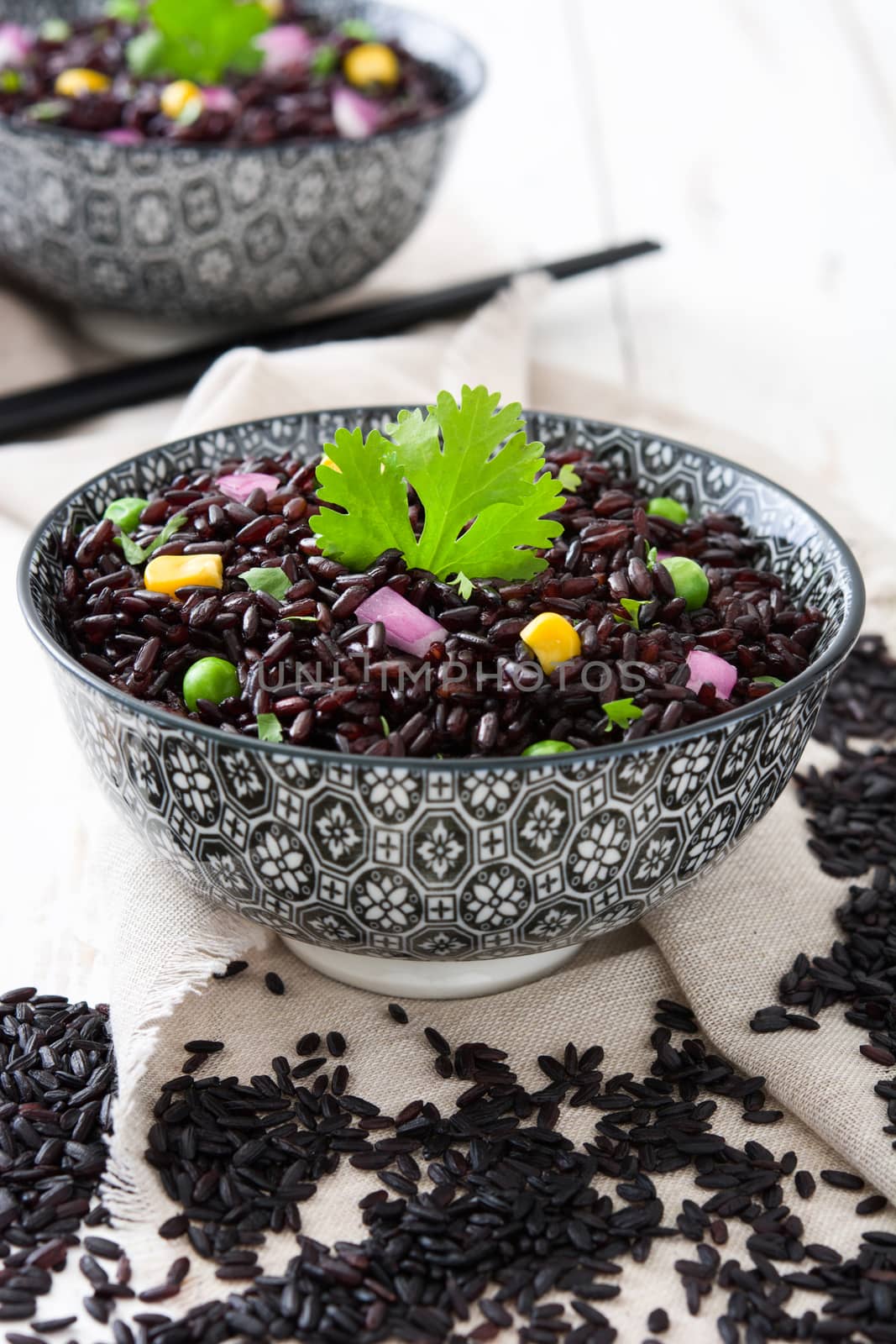 Black rice in a bowl and vegetables on wooden table