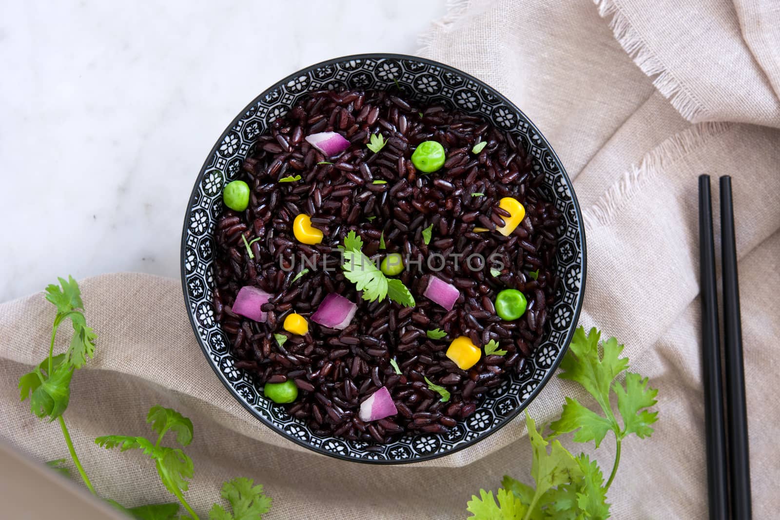 Black rice in a bowl and vegetables on white marble