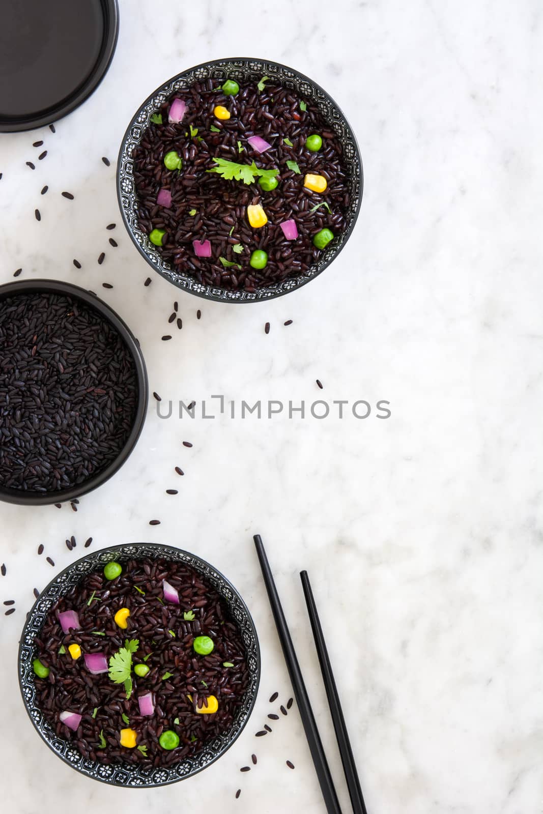 Black rice in a bowl and vegetables on white marble