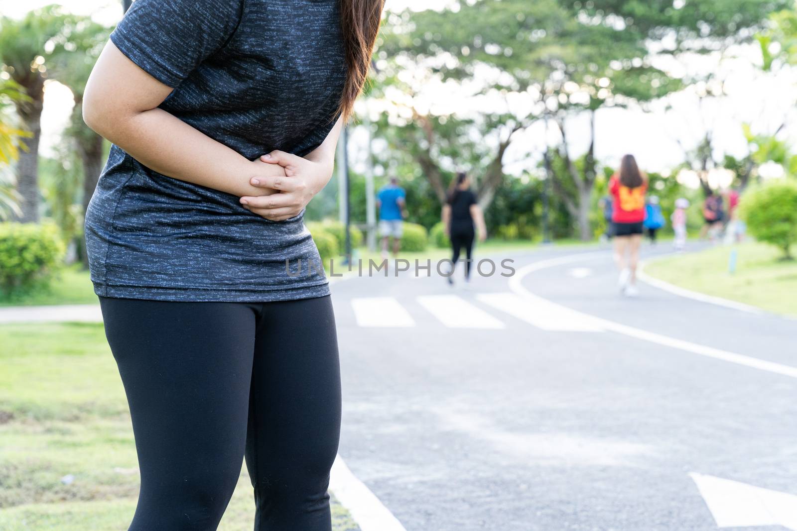 Asian woman suffering from stomach ache while running at the park. Injury from sport and exercise concept.