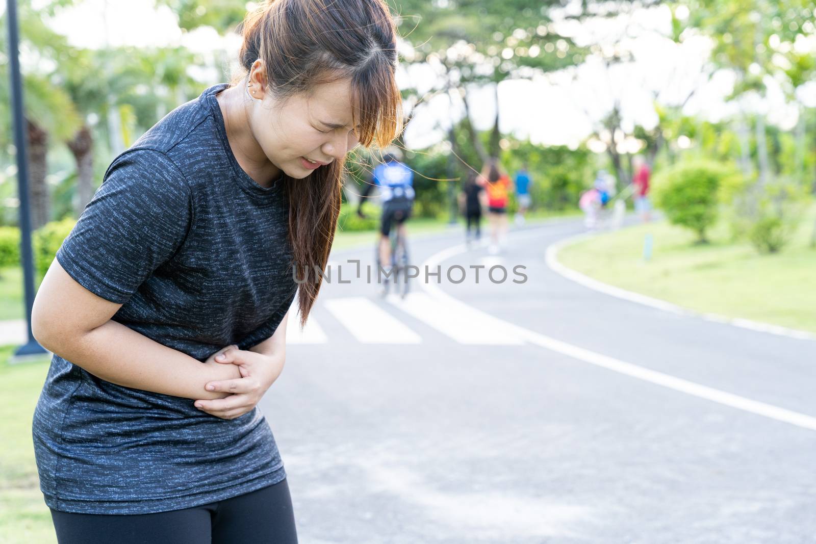 Asian woman suffering from stomach ache while running at the park. Injury from sport and exercise concept.