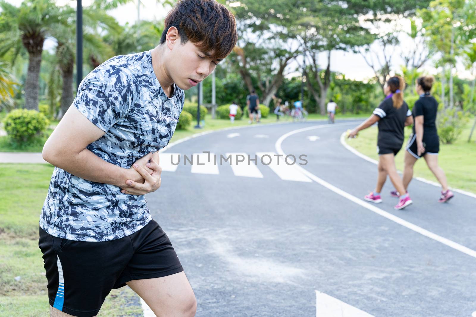 Asian man suffering from stomach ache while running at the park. Injury from sport and exercise concept. by mikesaran