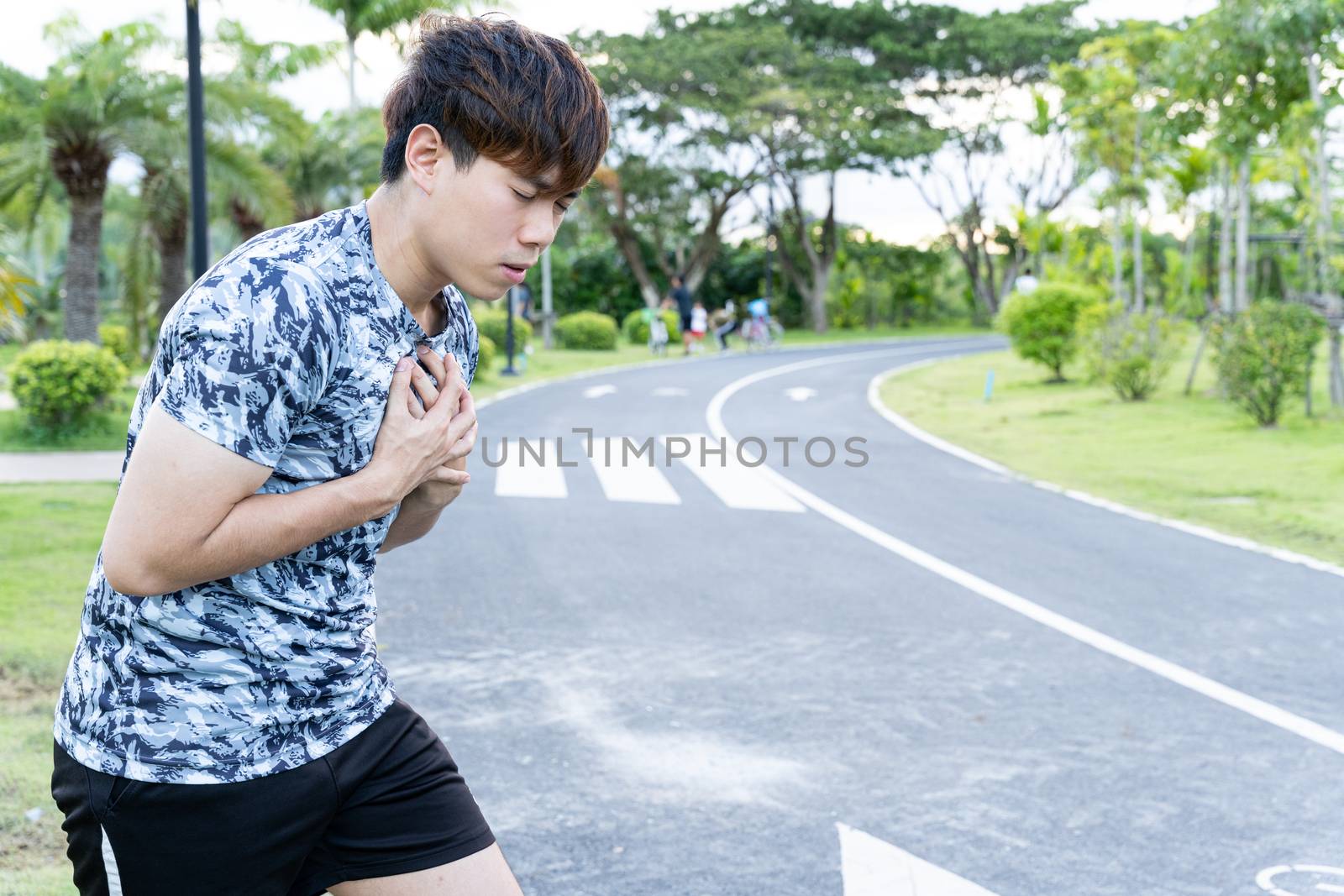 Exhausted male runner suffering painful angina pectoris or asthma breathing problems after running at the park. Sport and healthcare concept. by mikesaran