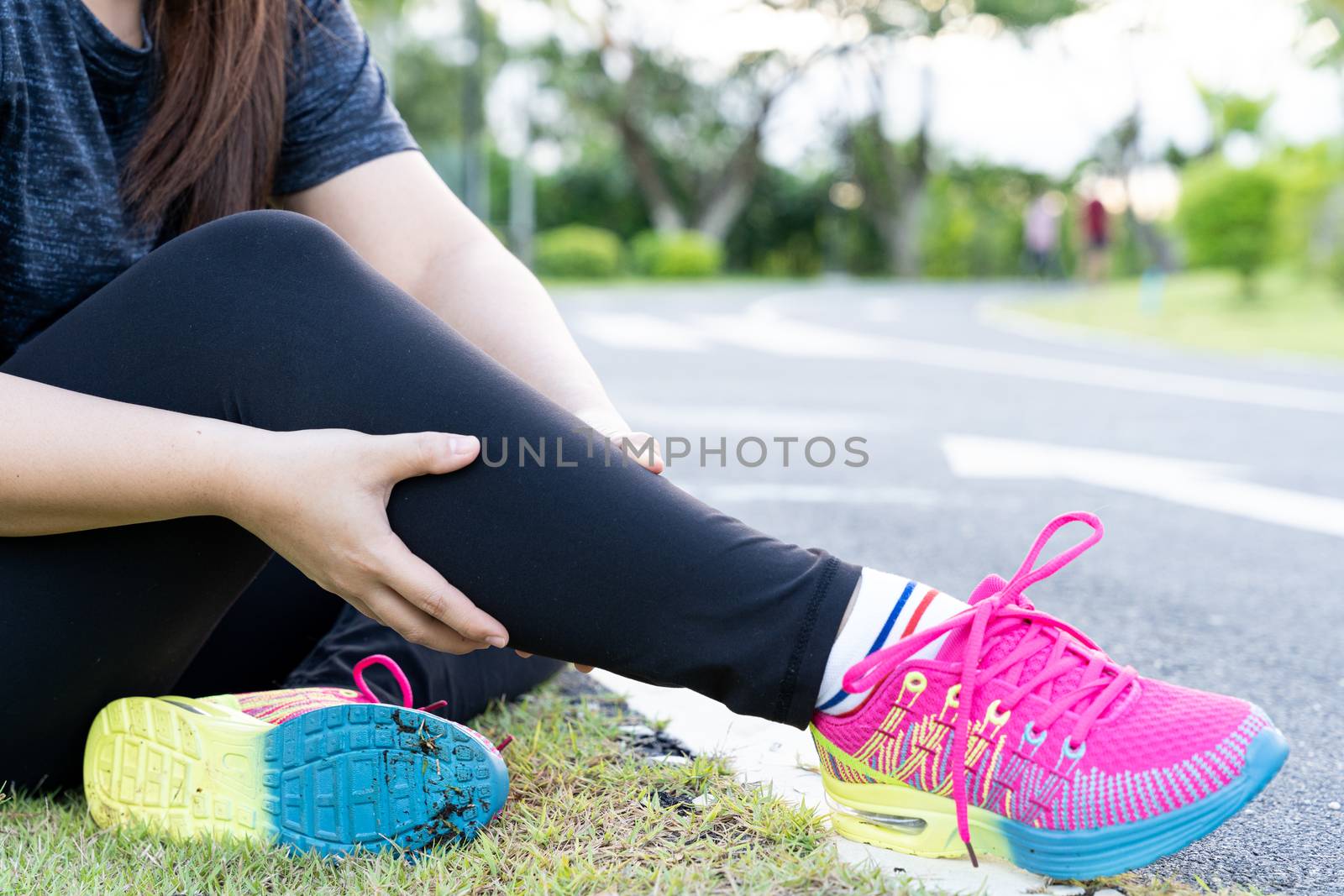 Asian woman massaging her painful calf ache from jogging and running outside at the park. Injury from sport and exercise concept.