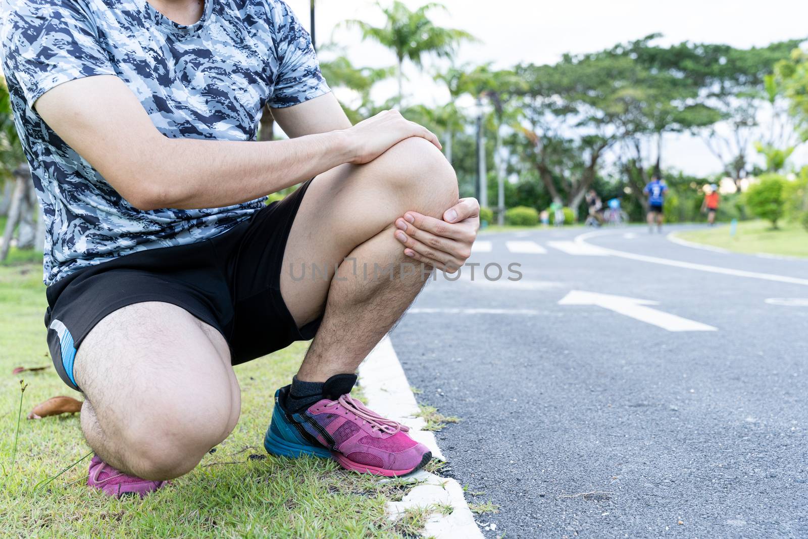 Asian man use hands hold on his knee injury while running on road in the park, Injury from workout concept.