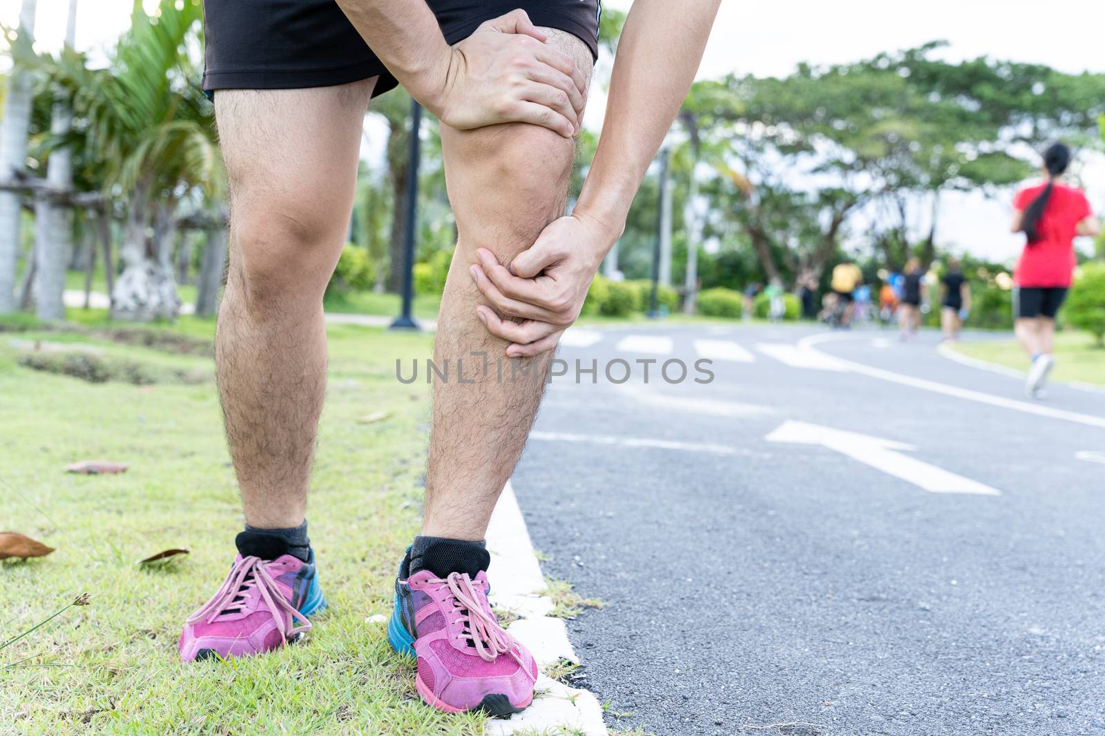 Asian man use hands hold on his knee injury while running on road in the park, Injury from workout concept.