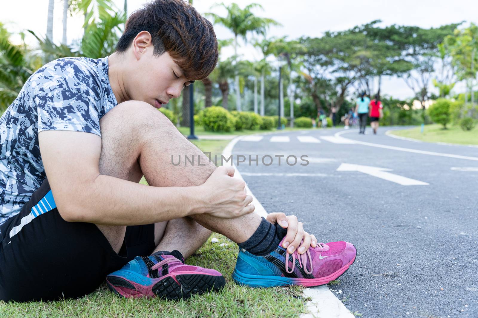Asian man use hands hold on his ankle while running on road in the park. Injury from workout concept.