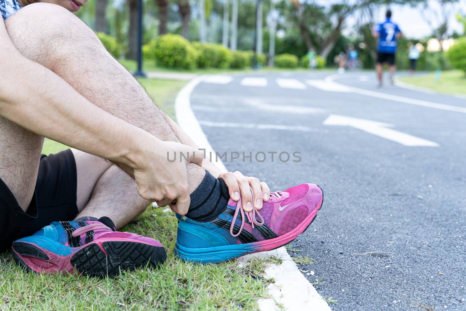 Asian man use hands hold on his ankle while running on road in the park. Injury from workout concept.