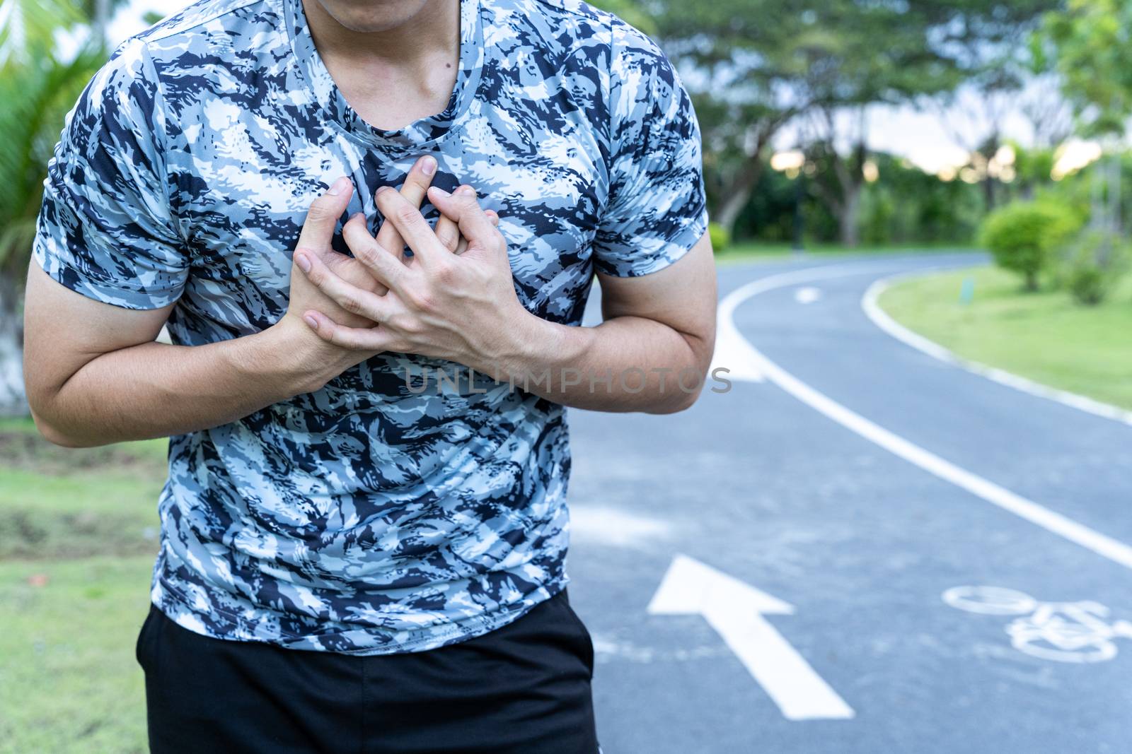 Exhausted male runner suffering painful angina pectoris or asthma breathing problems after running at the park. Sport and healthcare concept.